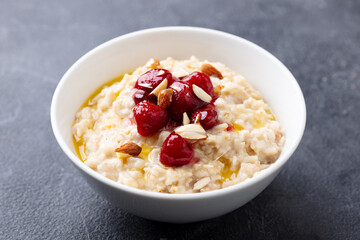 Oatmeal porridge with strawberry jam in white bowl. Grey background. Close up.