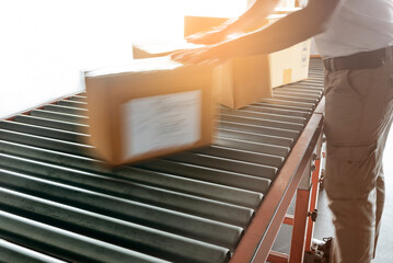 Warehouse worker sorting shipment package boxes on conveyor belt in distribution warehouse.

