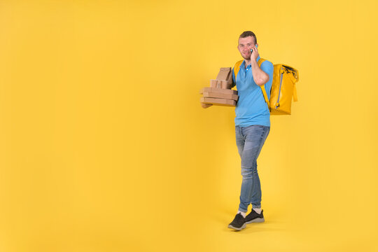 Delivery Guy In Blue Uniform Is Walking Talking On Phone Holding An Order With Food From Restaurant And Talking To Customer Behind His Back He Has Delivery Guy's Refrigerator Bag On Yellow Background