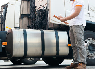 Truck driver holding clipboard inspecting safety tank fuel of semi truck, freight industry truck transport