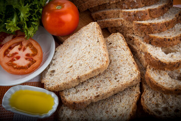 rebanadas de Pan de molde soja cerca con decoración de tomate y lechuga sobre madera y aceite de oliva