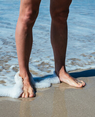 Man's feet standing on a beach at the ocean's edge