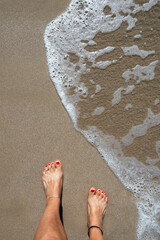 Woman's feet standing on a beach at the ocean's edge