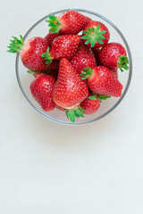 ripe strawberries of different sizes and varieties in a glass plate on a light wooden background, flat lay, copy space