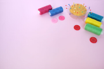 Sewing accessories colorful threads, pins and buttons on pink background with copy space. Flat lay