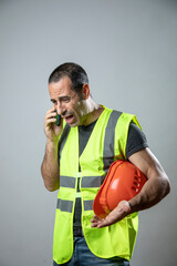 operaio con caschetto protettivo arancione e gillet giallo tenuto in mano fa una chiamata mostrando...