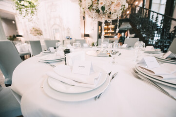 Restaurant, banquet, table setting. The table is covered with a white tablecloth, dishes, white clean plates, cutlery, napkins, wine glasses, candles. Close-up.