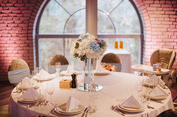 Restaurant, banquet, table setting. The table is covered with a white tablecloth, dishes, white clean plates, cutlery, napkins, wine glasses, candles. Close-up.