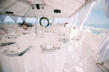 Restaurant, banquet, table setting. The table is covered with a white tablecloth, dishes, white clean plates, cutlery, napkins, wine glasses, candles. Close-up.