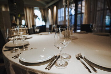 Restaurant, banquet, table setting. The table is covered with a white tablecloth, dishes, white clean plates, cutlery, napkins, wine glasses, candles. Close-up.