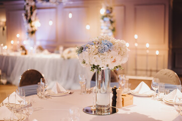 Restaurant, banquet, table setting. The table is covered with a white tablecloth, dishes, white clean plates, cutlery, napkins, wine glasses, candles. Close-up.