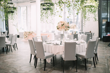 Restaurant, interior, banquet, table setting. The table is covered with a white tablecloth, dishes, white clean plates, cutlery, napkins, wine glasses, candles. Overall plan.