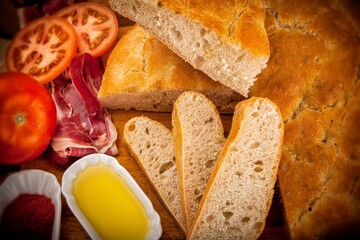 rebanadas de torta de pan artesanal de tahona con decoración  de tomate jamón y aceite sobre madera y mantel 