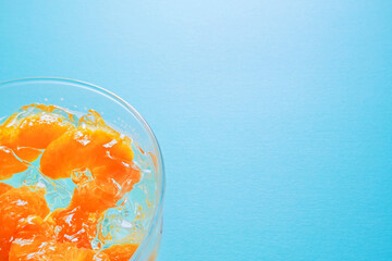青背景の左寄りに透明のガラスの器に入れた砕けたみかんゼリーとコピースペース