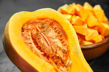 Chopped butternut squash, pumpkin half, fresh vegetable pieces in wooden bowl on black stone table