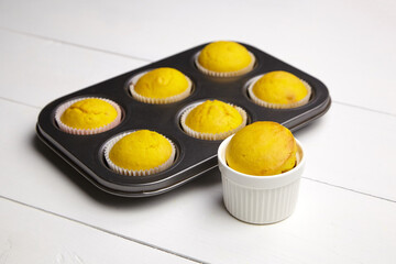 Pumpkin cupcakes in white ceramic ramekin baking bowl and 6-slot steel baking tray on white wooden table