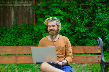 Fototapeta premium Man with laptop at park. Smiling man working on laptop outdoors. Man sitting outside with laptop. Freelance. Study and work online. Online work.