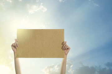 Woman's hands holding a blank banner to put the text at protesting with clear sky and sunlight...