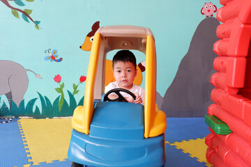 An Asian boy wearing a white shirt is playing a toy car in the playground.