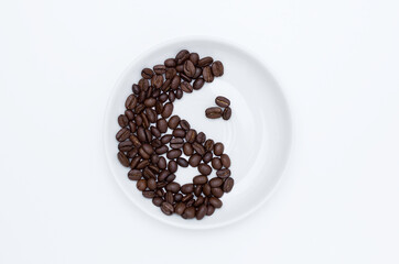Yin Yang sign of coffee beans on a white saucer top view, white background. Concept of the pleasure of drinking coffee.