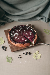 Round blueberry pie sprinkled with powdered sugar cut on a wooden board on the table on a gray background. A piece is taken with a spoon.	