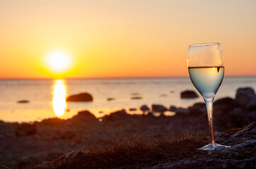Wine glass standing on a cobblestone beach with ocean sunset background