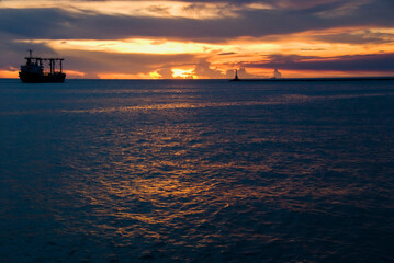 Naklejka na ściany i meble Sunset into the sea with the container ship silhouette.