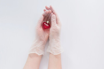 Red heart of red glass in a woman's hands on transparent protective gloves. Protect, health. Coronavirus, COVID-19.