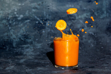 Fresh carrot juice splash in glass on a dark background
