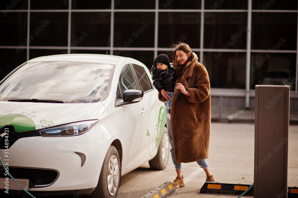 Wall mural young mother with child charging electro car at the electric gas station.