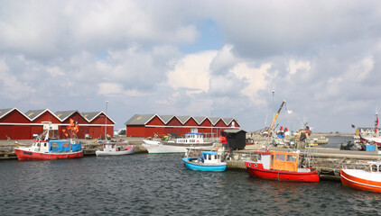 Fototapeta na wymiar Several colorful fishing boats in the small port of Hasle on the west coast on the Danish island of Bornholm in the Baltic Sea. It is a sunny day with nice clouds with some wind and waves.