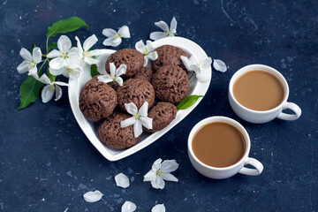 Spring composition with apple tree flowers and homemade chocolate cookies. Dessert for served for coffee break on a heart shaped plate. Snack on a spring day in the garden