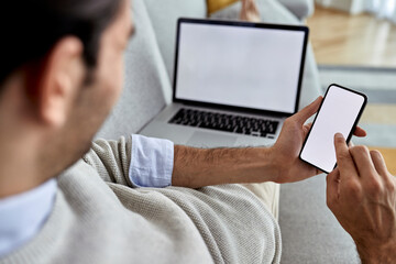 Close-up of man using mobile phone while working on laptop at home.