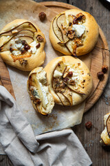 Homemade hand pizzas with pear, ricotta, gorgonzola and hazelnuts on round wooden board.