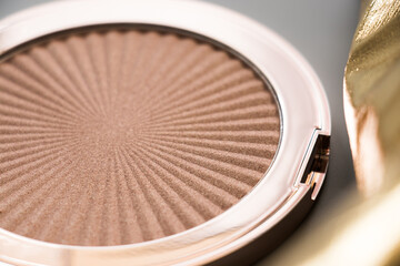 Highlighter, for face, makeup. Beautiful highlighter for your best makeup and a part of gold element on a grey background.
