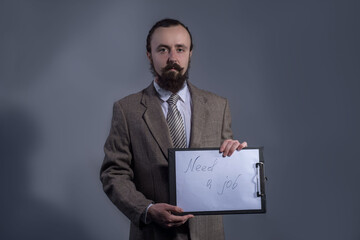 Portrait of a man of thirty, in a business suit, is holding a table with the inscription need job. Studio photo on a gray background.