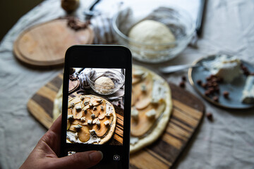 Step by step process of making homemade pizza with pear, ricotta, gorgonzola and hazelnuts. Taking photo of uncooked pizza on smartphone.