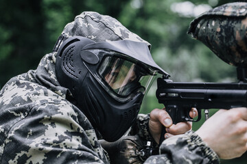 Closeup Portrait of Paintball Player In Full Gear At The Shooting Range with Paintball marker in...