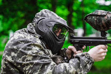 Closeup Portrait of Paintball Player In Full Gear At The Shooting Range with Paintball marker in...