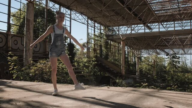 Girl teenager athlete gymnast doing somersault jump freestyle hovering in air on background of rusty metal structures of an abandoned building slow motion in summer. Fitness. Sport. Athletics