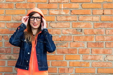 Fototapeta na wymiar Happy young woman in a denim jacket, clothes glasses on a background of a red brick wall