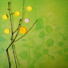 Square photo of spring twigs and paper flowers lying on top of floral green sheet of scrapbooking paper.  Small sticker with the word spring in lower part of image. Copy space to the right.
