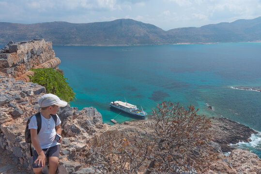 White little boy lookig at cruise ship and beach with magical turquoise waters, lagoon on Crete, Greece. Family holiday concept.