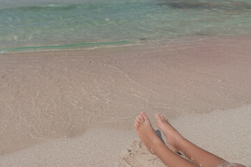 Child feet on the pure white and pink sand beach with magical turquoise waters, in lagoon on Crete, Greece. Family holiday concept