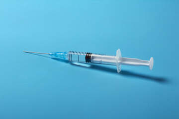 The syringe with the vaccine on a blue background is lying sideways