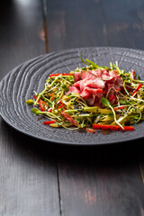 Authentic salad with bacon fresh red pepper, sprouts, sesame and olive oil on a black plate. Morning atmospheric lighting, fashionable trendy spot soft focus. Preparation for design creative menu.