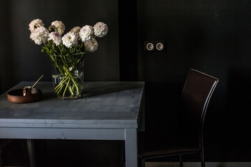 Interrior fragment of the dark room with grey table, brown chair, vaze with dahlia flowers and coffie