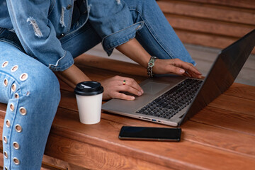 The girl with dark hair in a white medical mask and blue jeans. Young european woman with laptop working outdoors. New life concept for students and freelancers. Remote work