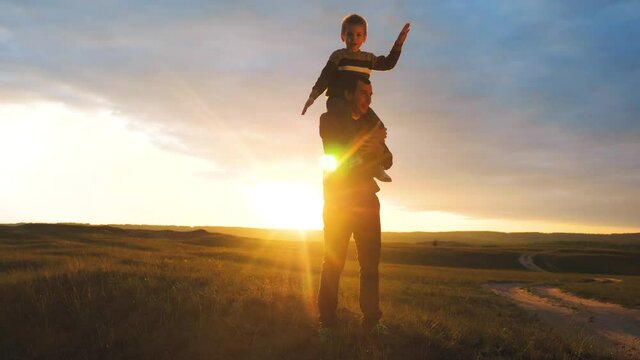happy family. son sits on his neck teamwork at father shows hands to the side plays at the pilot depicts an airplane silhouette at sunset. happy family concept childhood man lifestyle dad with little