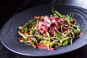 Authentic salad with bacon fresh red pepper, sprouts, sesame and olive oil on a black plate. Morning atmospheric lighting, fashionable trendy spot soft focus. Preparation for design creative menu.
